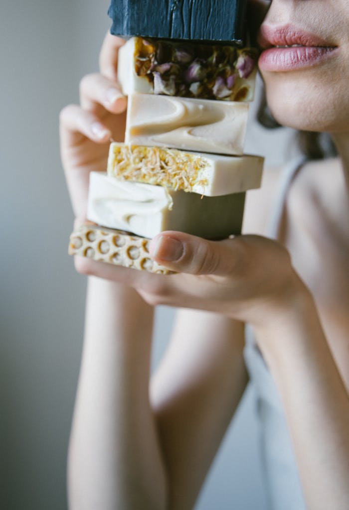 Close-up of a woman's hands holding stacked artisanal soap bars, showcasing their textures.